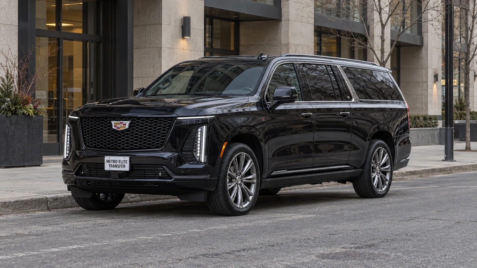 A black Cadillac Escalade ESV with a Metro Elite Transfer plate outside a stone-and-glass commercial building
